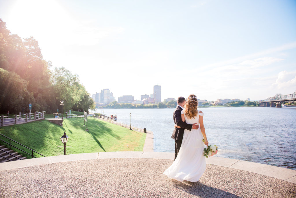 Bride and groom embracing on a lookout overlooking the Ottawa River near the Bytown Museum and Byward lockstation, with the city skyline across the water.