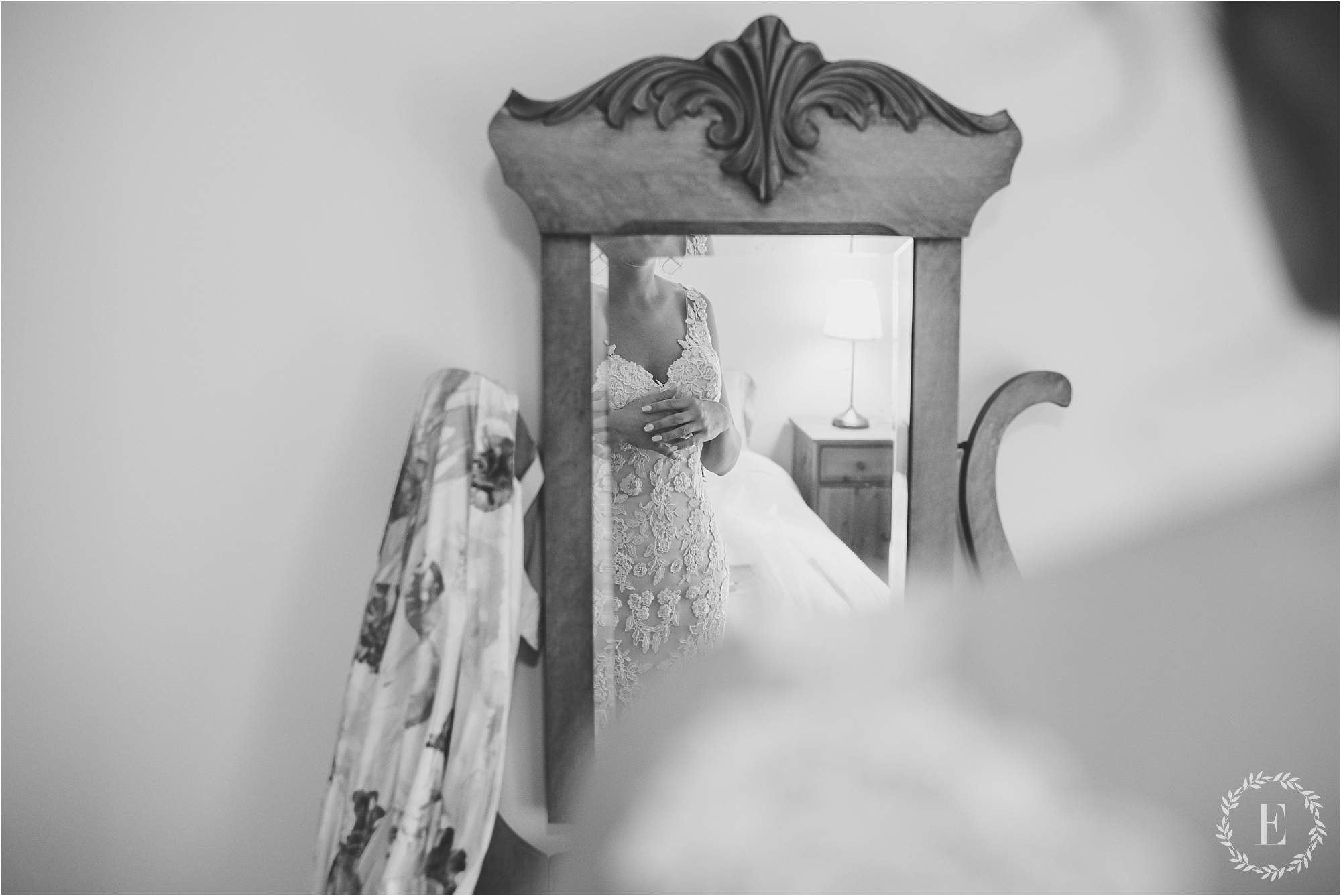 Black and white photo from Revelle Bridal showing a bride's reflection in an antique wooden mirror as she adjusts her lace gown