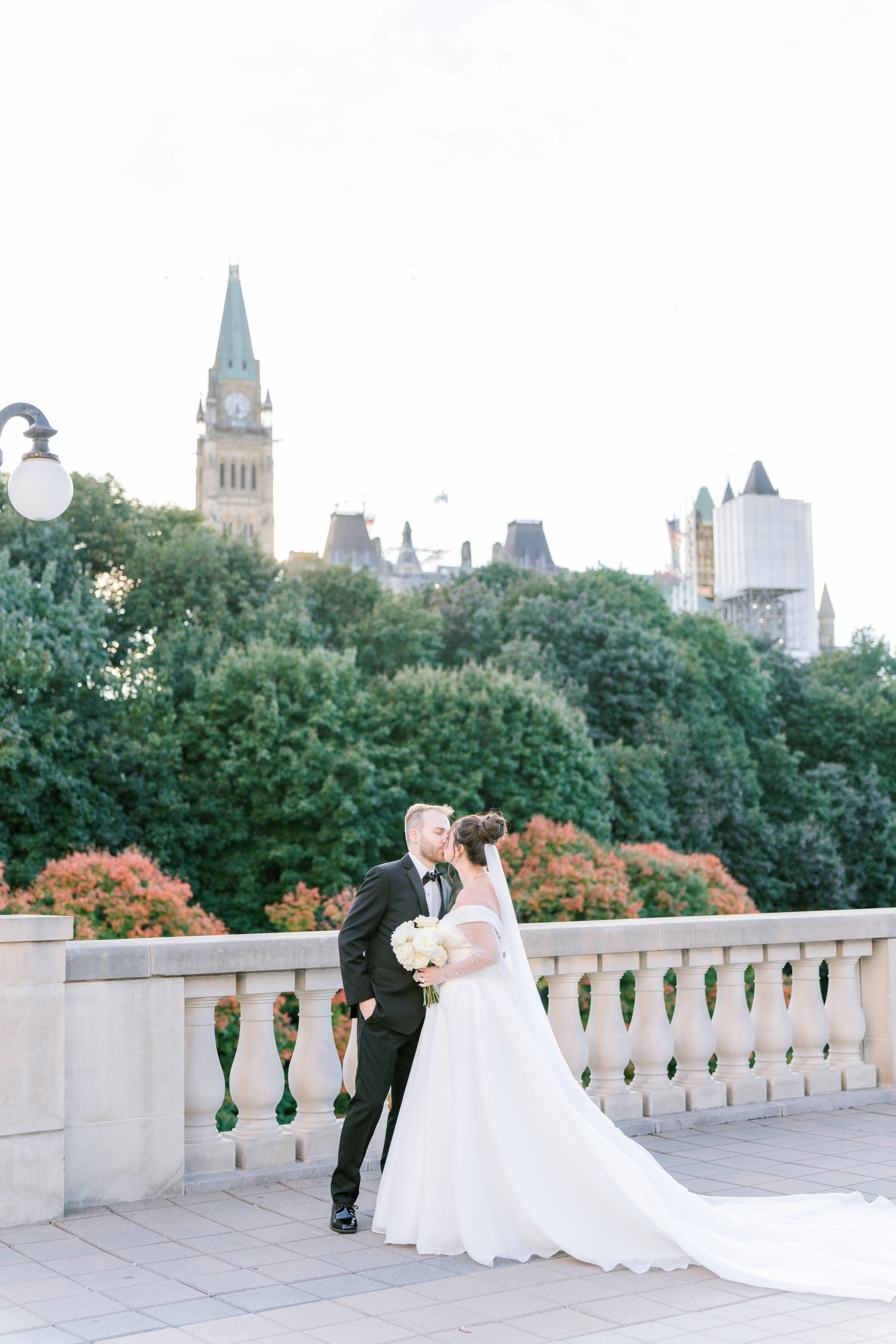 Bride and groom admiring the view from a stone balcony near the National Arts Centre (NAC), with Ottawa's Peace Tower rising above the tree line.