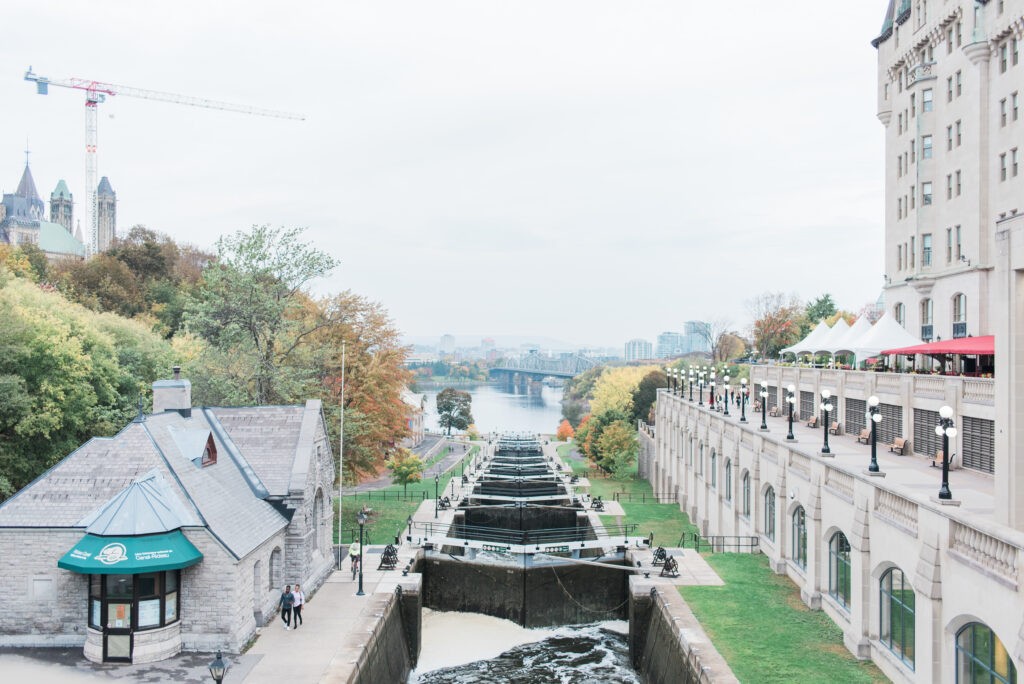 View down the Rideau Canal locks at the Byward lockstation in Ottawa, with the Bytown Museum on one side, the Château Laurier on the other, and Parliament visible in the distance.
