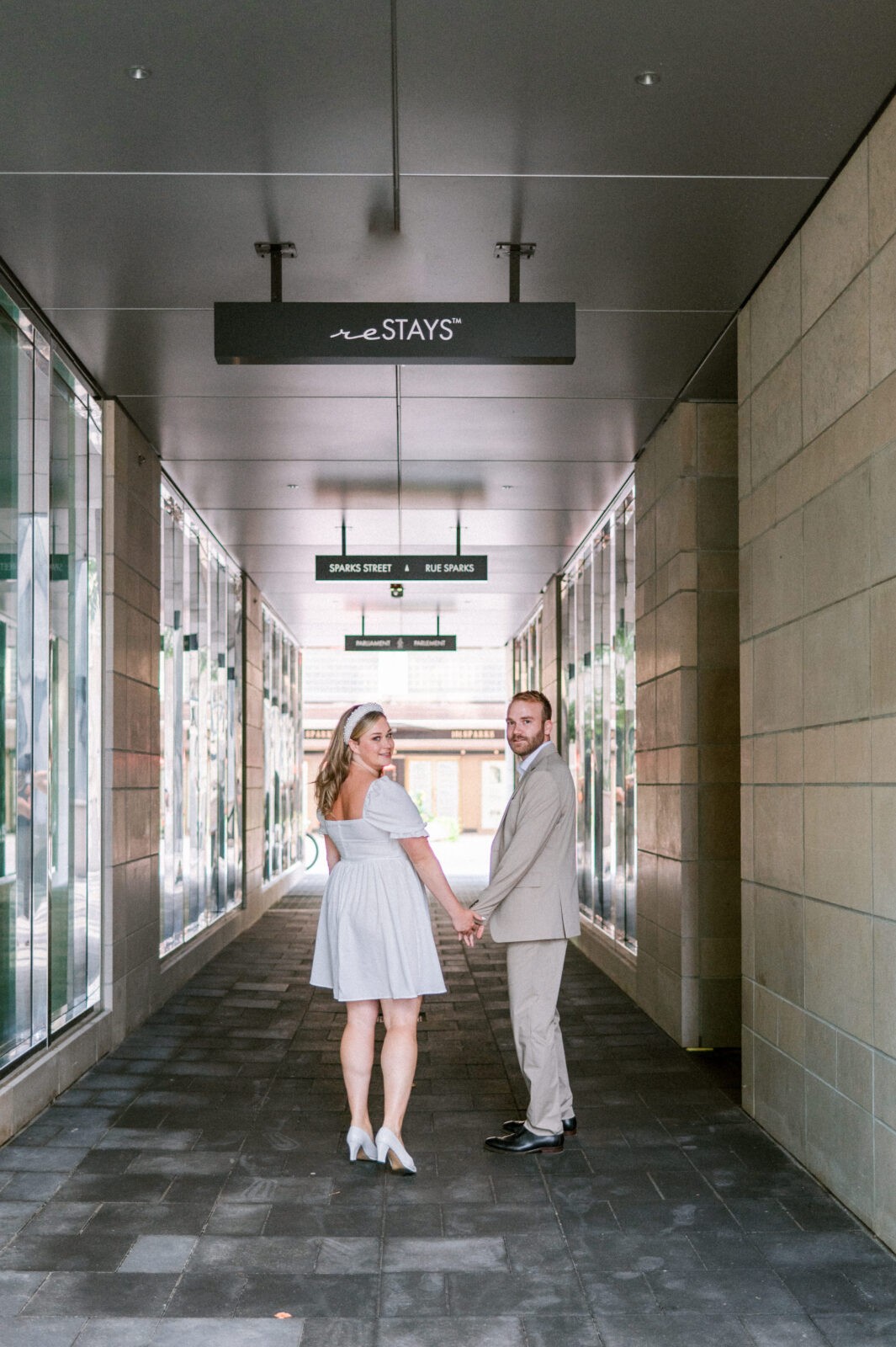 Couple holding hands and walking through a modern city passageway.
