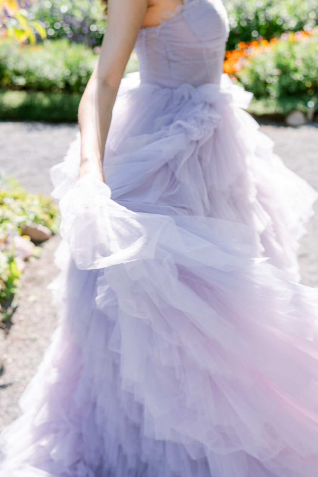 Close-up of a lavender tulle ball gown from Chic Bridals with ruffled layers, worn by a model standing in a sunlit garden
