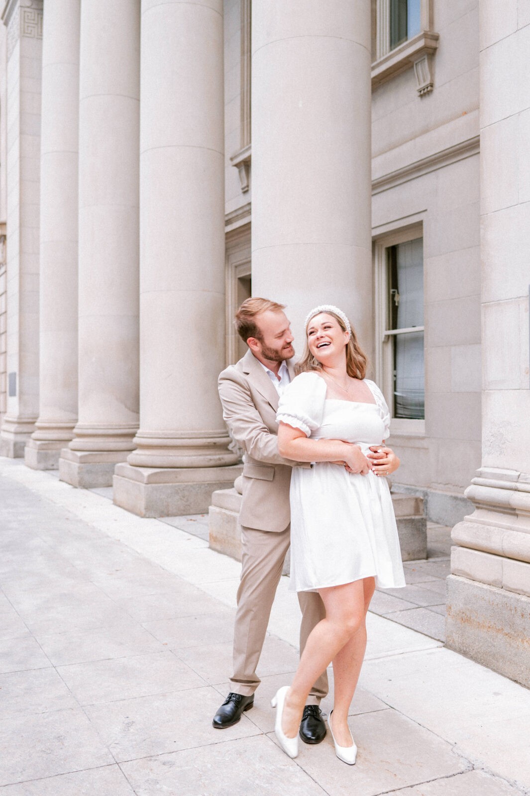 Couple laughing together while embracing beside classic columned architecture.