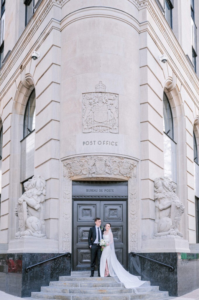 Bride and groom on the stone steps of the Canada Post building on Sparks Street, Ottawa, framed by carved lions and the Post Office entrance.