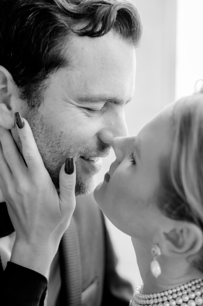 Black and white close-up of a couple sharing an intimate moment, the woman cupping the man's face as they lean in close with eyes closed.