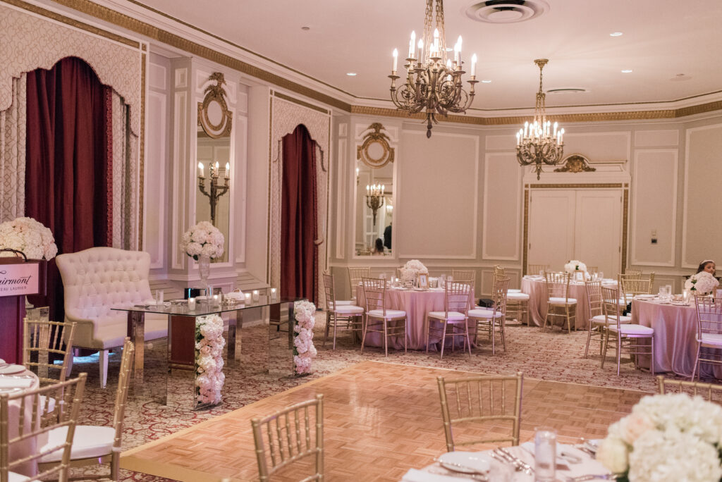 Reception setup in the Drawing Room at the Fairmont Château Laurier, with pink linens, gold chiavari chairs, a mirrored sweetheart table with floral accents, and ornate candle chandeliers.