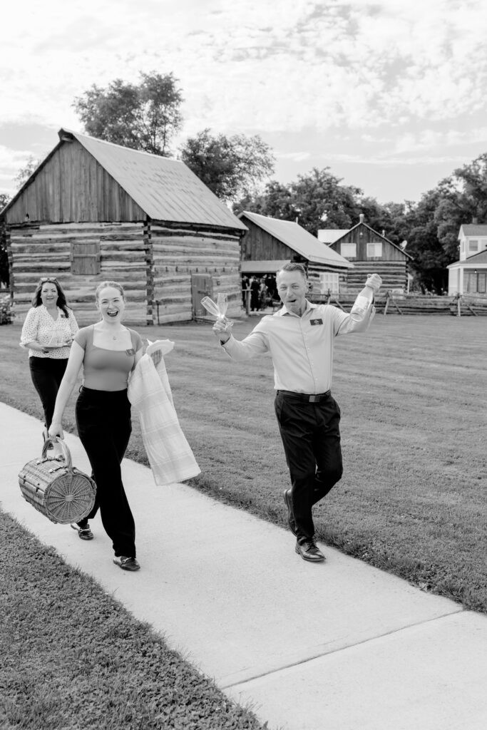 Black and white photo of guests walking along a path near a log cabin at Stonefields Estate, one waving joyfully.