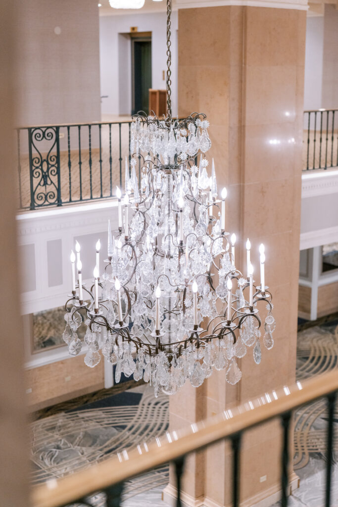Crystal candle chandelier hanging above a stone balcony at the Fairmont Royal York, with wrought-iron railings and patterned carpet visible below.