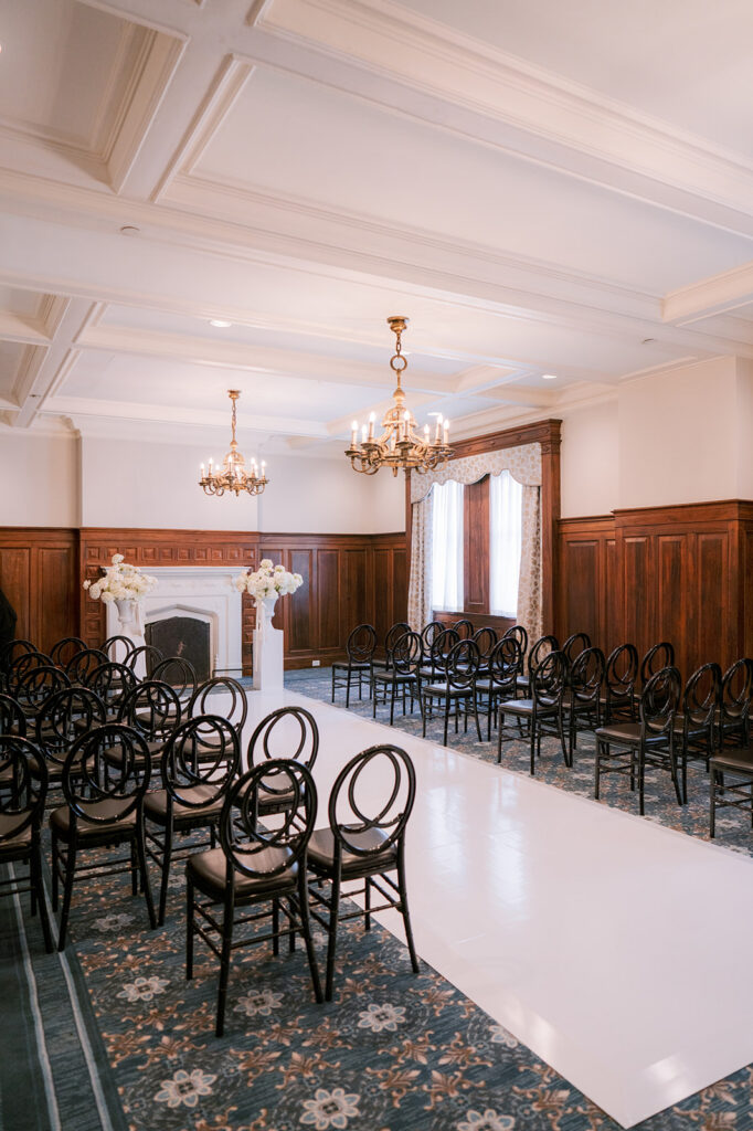 Wedding ceremony setup at the Fairmont Château Laurier with dark bentwood chairs lining an aisle beneath a coffered ceiling and brass chandelier.