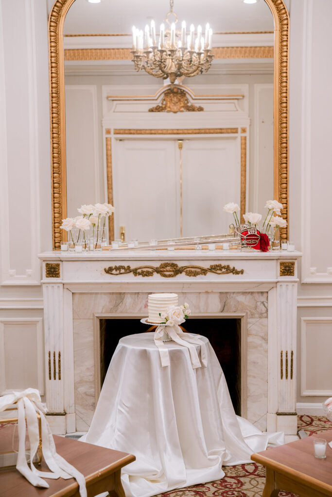 Elegant marble fireplace mantel at the Fairmont Château Laurier, adorned with a gilt-framed mirror, chandelier, and a draped cake table set beside it.