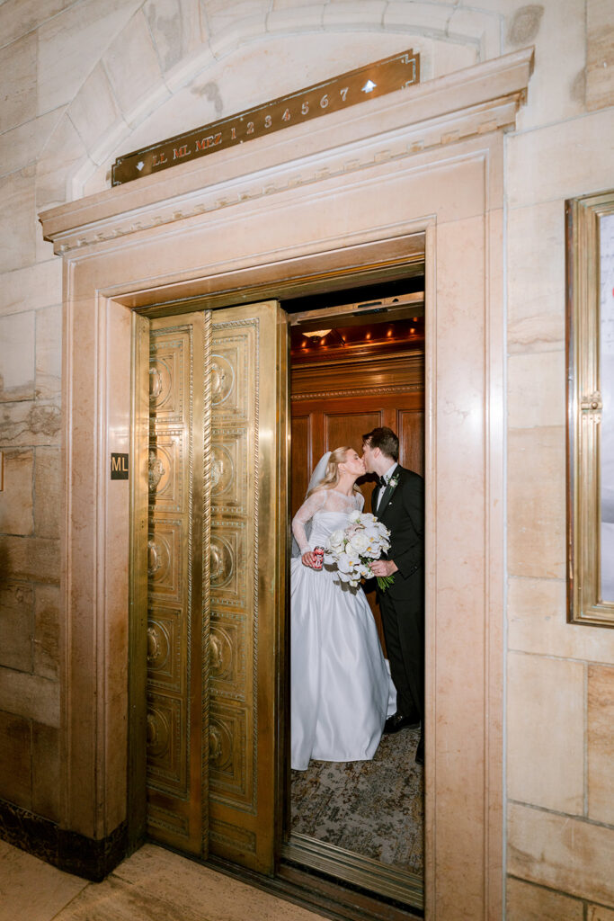 Bride and groom sharing a kiss inside a vintage brass elevator with wood-paneled interior at the Fairmont Château Laurier.