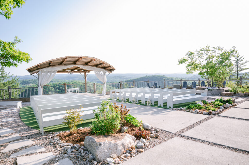Outdoor ceremony space at Le Belvédère with white benches leading to an arbor overlooking rolling hills and countryside views.