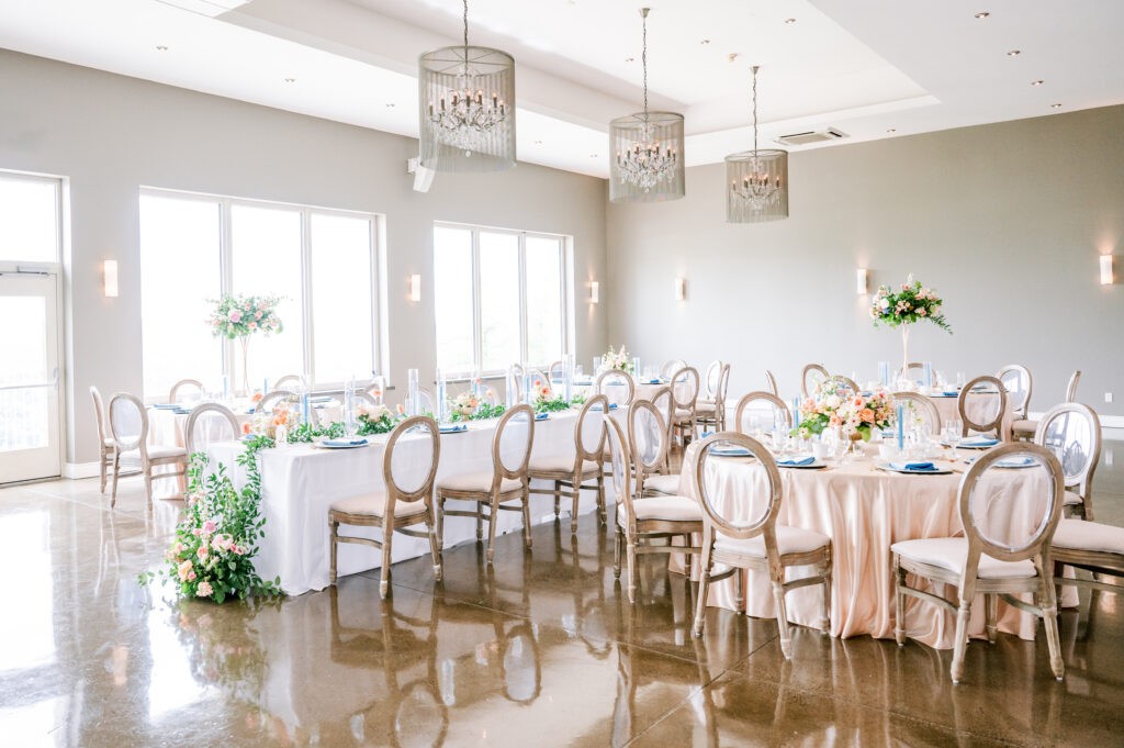 Reception dining room at Le Belvédère with oval-back wooden chairs, a long table set in blue and white linens, and crystal drum-shaped chandeliers overhead.