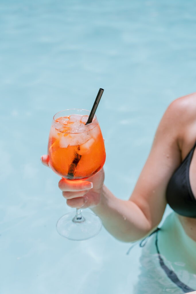 Woman in a pool holding an Aperol spritz style cocktail, part of a wedding weekend in Italy.