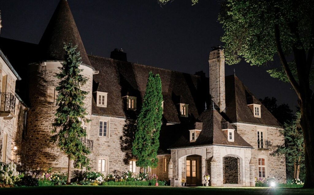 Château style stone manor lit up at night with steep turret roofs and lush gardens, Eaton Hall (King City), a fairytale Old World European wedding venue in Canada.