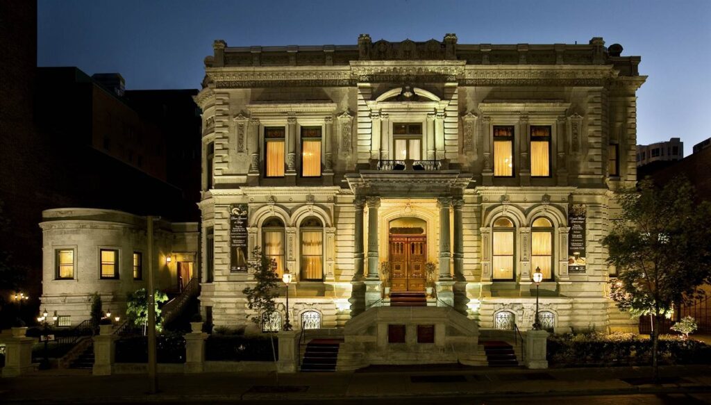 Ornate stone mansion glowing with warm light at dusk, featuring arched windows and a grand columned entrance, Le Mount Stephen (Montreal), a historic Old World European wedding venue in Canada.