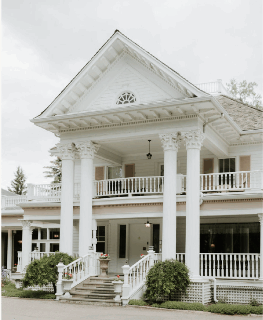 Exterior view of The Norland Historic Estate in Lethbridge, a white colonial-style mansion with grand columns, a wraparound porch, and a second-floor balcony.