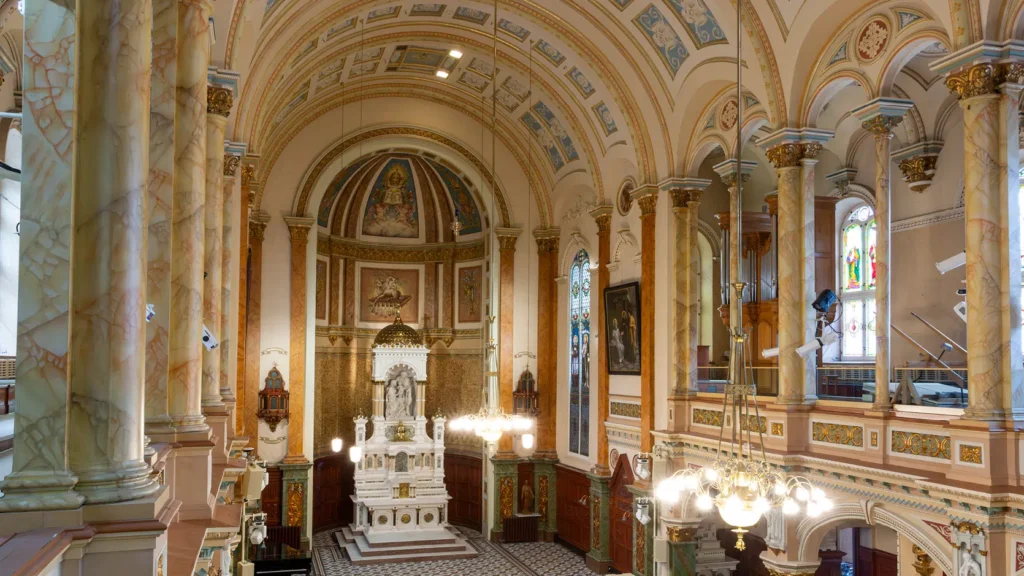 Ornate interior of the Chapelle du Séminaire, featuring a marble altar, painted vaulted ceilings, marbled columns, and stained glass windows.