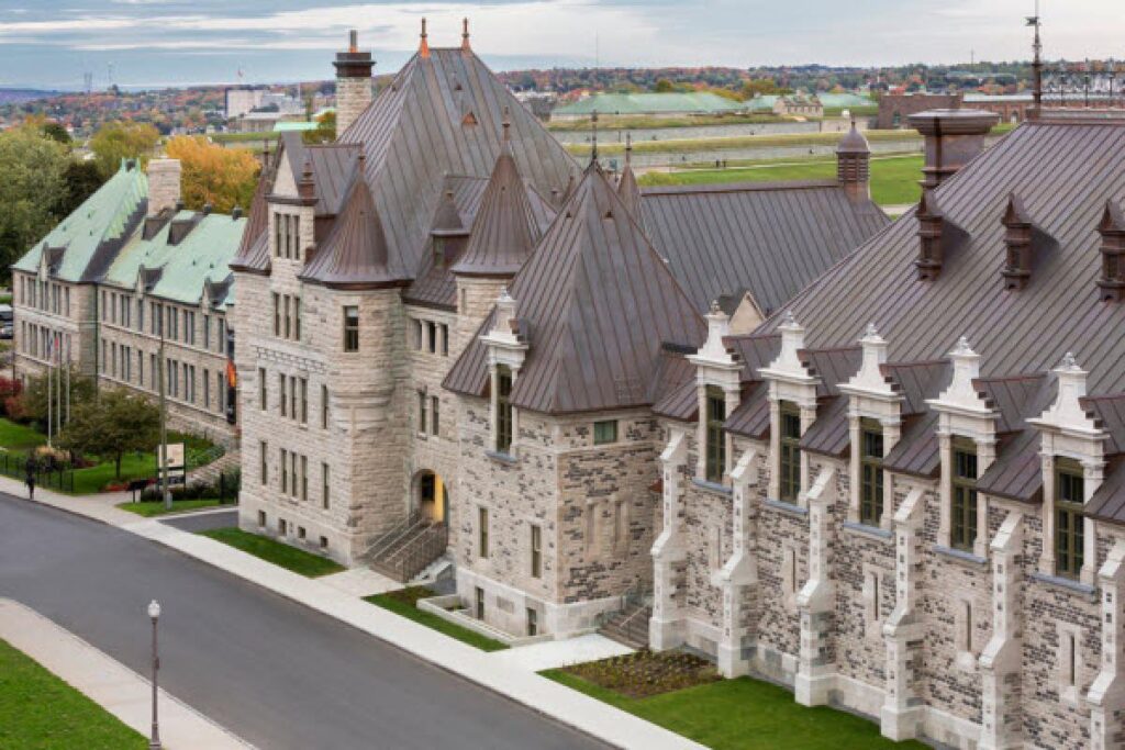 Aerial view of the Manège Militaire Voltigeurs de Québec, a historic stone armoury with turreted towers and steep copper roofs overlooking the surrounding cityscape.