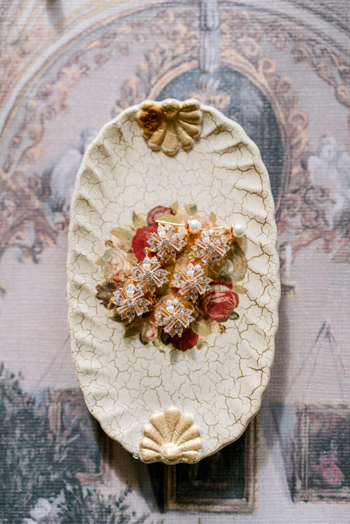 Vintage floral brooches with pearl accents arranged on a crackle-glazed ceramic dish with shell details.
