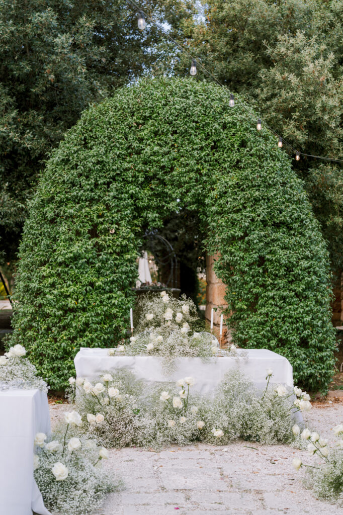 Lush ivy-covered archway framing a stone altar dressed with white floral garlands, styled by Amelia at A. Carleton Weddings.