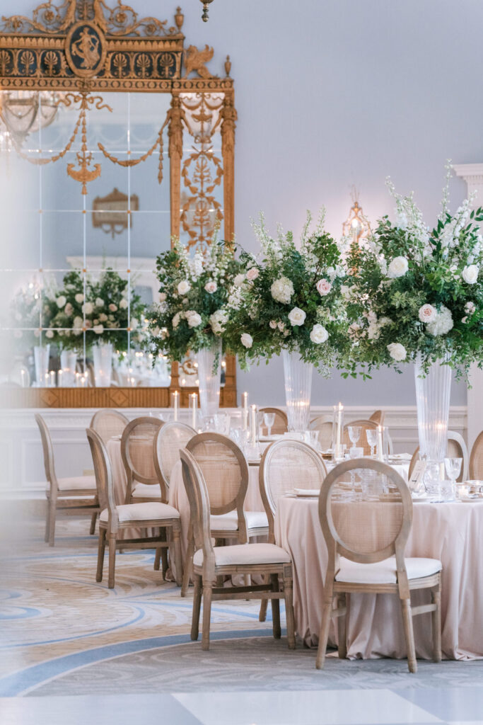 Elegant reception room with gilded mirror backdrop, tall white floral arrangements, and upholstered chairs on a checkered marble floor, styled by Erica Irwin Weddings & Events.