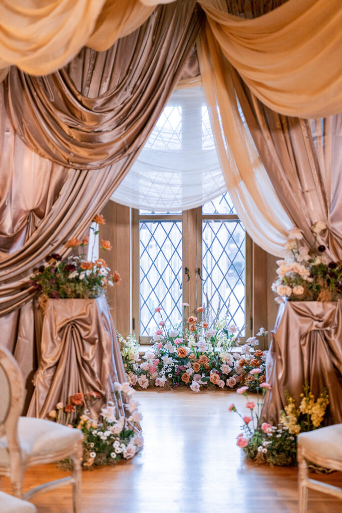 Close-up view of the draped ceremony backdrop and floral-adorned chairs beside leaded-glass windows.