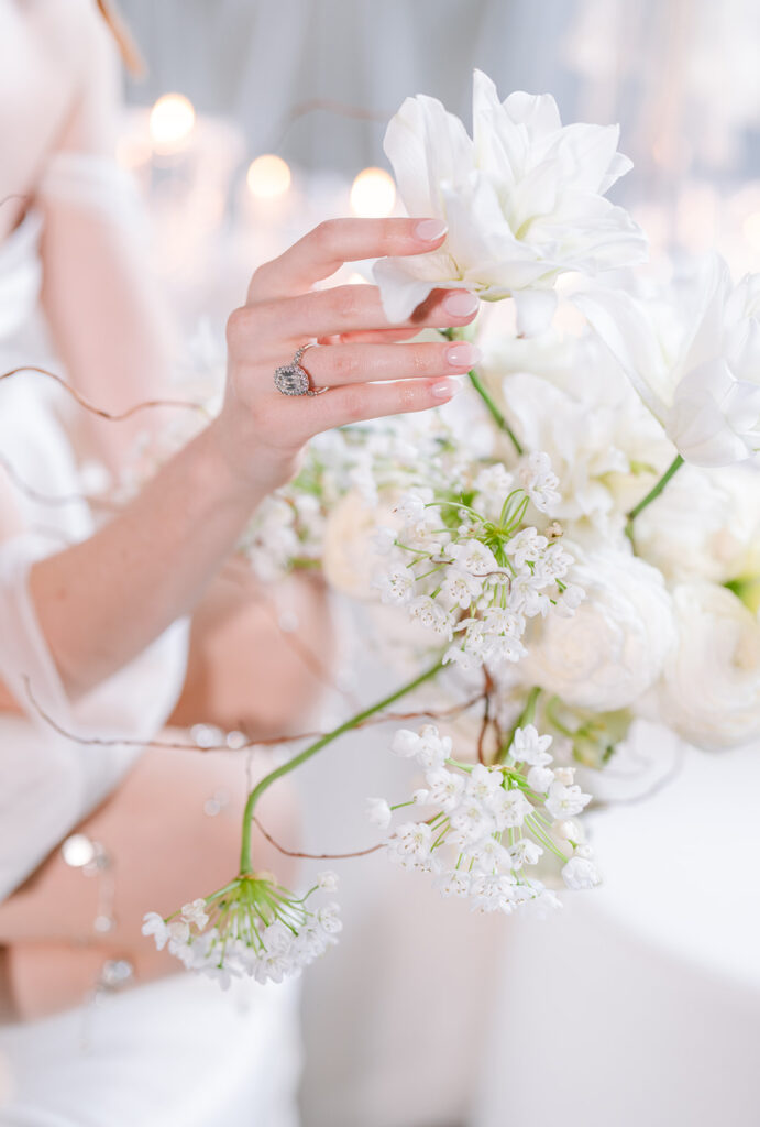 Close-up of a bride's hand adjusting white floral stems, with soft candlelight in the background, styled by Elise at Toast Events.