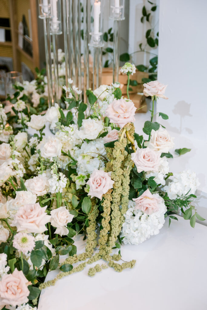 Close-up of blush and white rose arrangement with trailing amaranthus, styled beside tall glass taper candle holders, styled by Amanda Simplice.