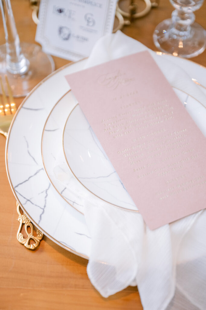 Elegant place setting with a marble-patterned charger plate, gold rim details, and a blush embossed menu card, styled by Amanda Simplice.
