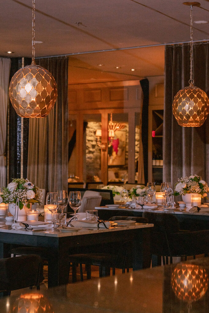 Intimate dining room with dark marble tables, white florals, and glowing amber globe pendant lights, styled by Cindy and Rita at All In Event Planning & Design.
