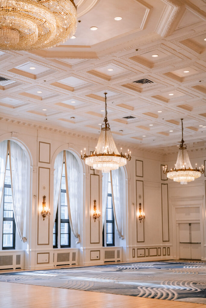 Elegant empty ballroom at Fairmont Royal York in the Financial District, featuring crystal chandeliers, a coffered ceiling, arched windows with sheer drapes, and wall sconces.