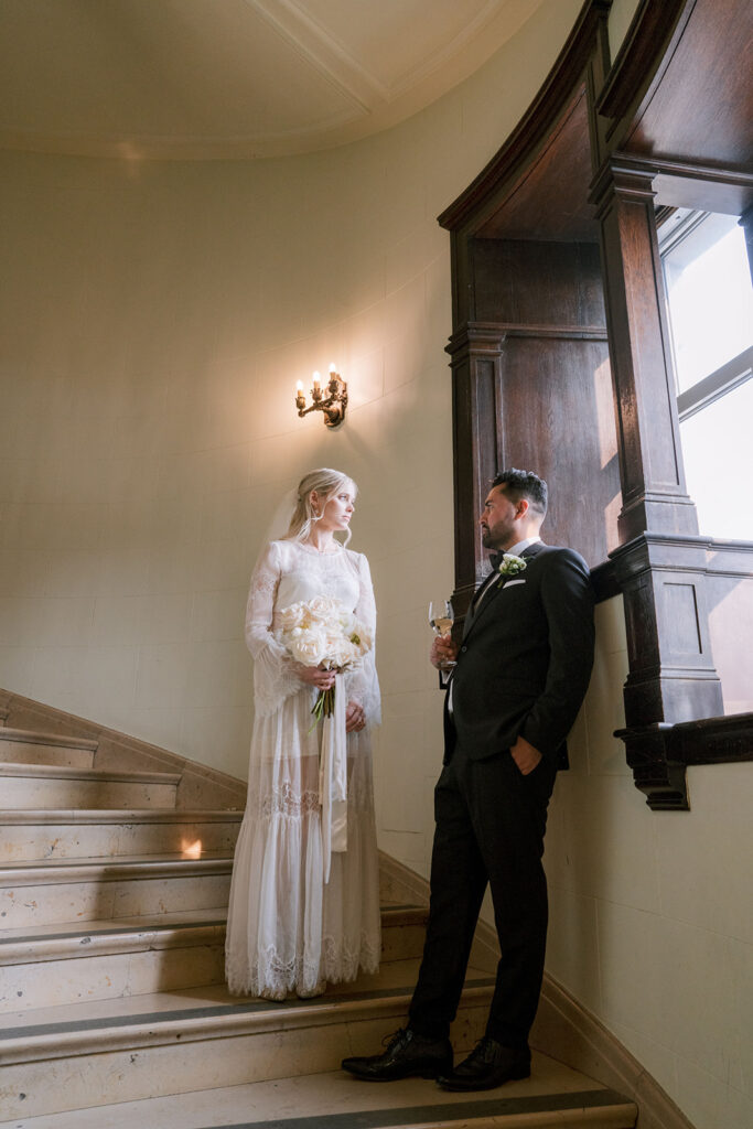 Bride and groom on a stone staircase beneath a wall sconce at the Fairmont Château Laurier, Ottawa — photographed by Emma Haidar