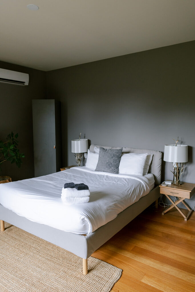 Grey-walled guest bedroom with a white bed, table lamps, and a jute rug at Compass Rose, a Prince Edward County wedding venue