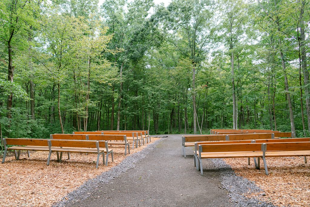 Woodland ceremony space with rows of wooden benches along a gravel aisle at Compass Rose, a Prince Edward County wedding venue