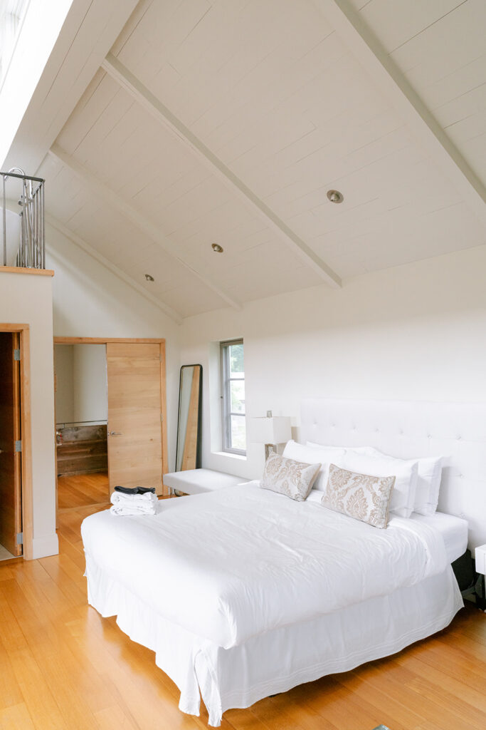 Bright bedroom with a white bed and vaulted wood-panel ceiling in the accommodations at Compass Rose, Prince Edward County