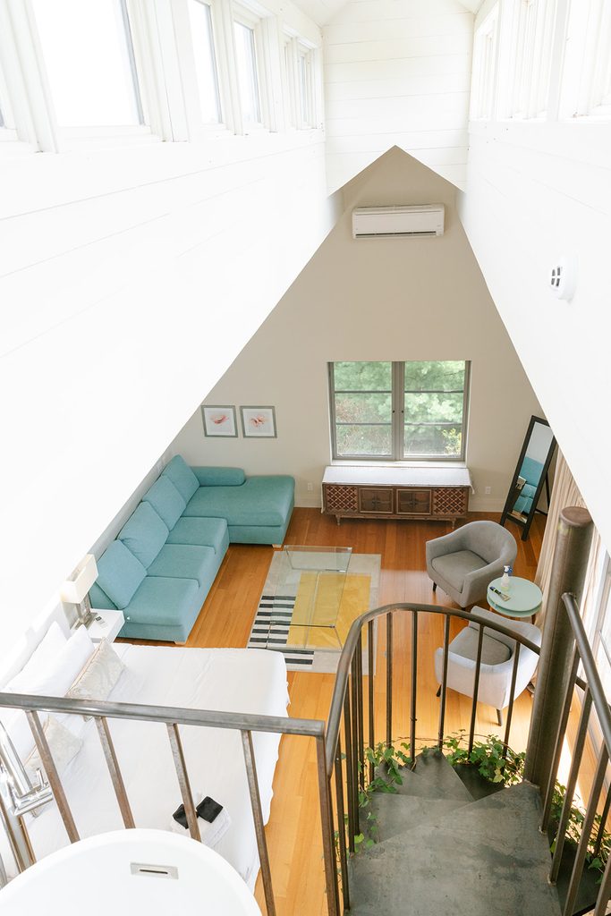 Loft lounge with a teal sectional and spiral staircase under a peaked ceiling at Compass Rose in Prince Edward County