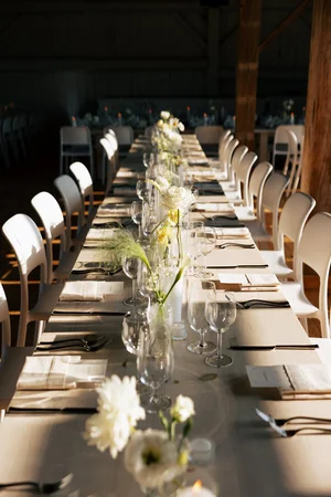 Long wedding reception table with white chairs, bud vases of white blooms, and warm sunlight, styled by Lexington and Co, Toronto wedding planner.
