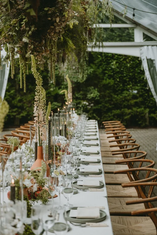 Long tented wedding reception table with wooden wishbone chairs, terracotta vases, and a hanging greenery installation, styled by Lexington and Co, Toronto wedding planner.