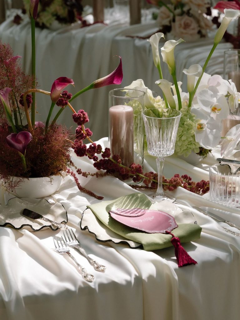 Wedding place setting with burgundy calla lilies, white orchids, crystal glassware, and a sage green napkin, styled by Kristen Ross of Mildred and Co, Prince Edward County wedding planner.