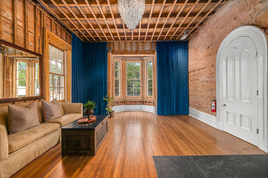 Robbie Burns Room at The Cape, featuring exposed brick walls, a wooden ceiling, rich hardwood floors, deep blue drapes, and a cozy lounge seating area.